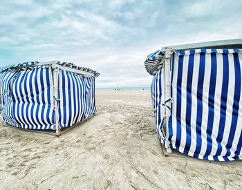 Hooded chairs on beach against sky