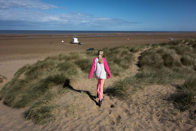 Rear view of girl walking at beach against sky during sunny day