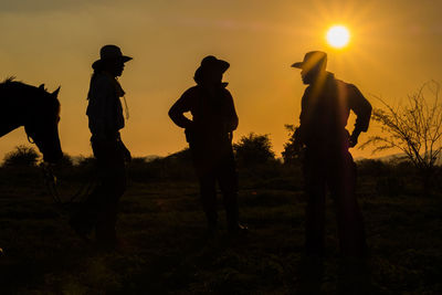 Silhouette people standing on field against sky during sunset