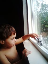 Shirtless boy playing with toy motorcycle on window at home