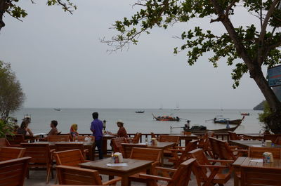 People on table by sea against clear sky