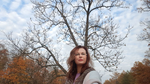 Low angle portrait of young woman against bare tree