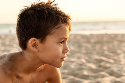 Close-up portrait of shirtless boy at beach against sky