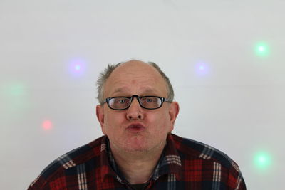 Portrait of mature man wearing eyeglasses while puckering against wall