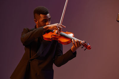 Midsection of man playing violin against wall