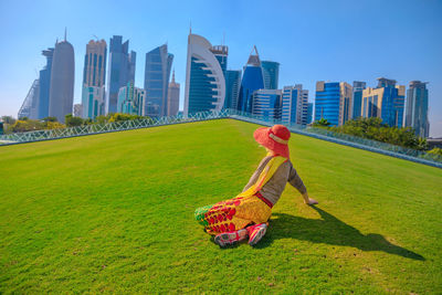 Woman sitting on field against modern buildings