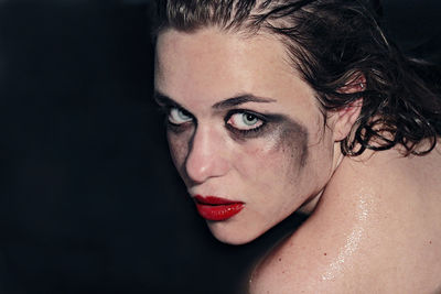 Close-up portrait of shirtless female model with make-up against black background