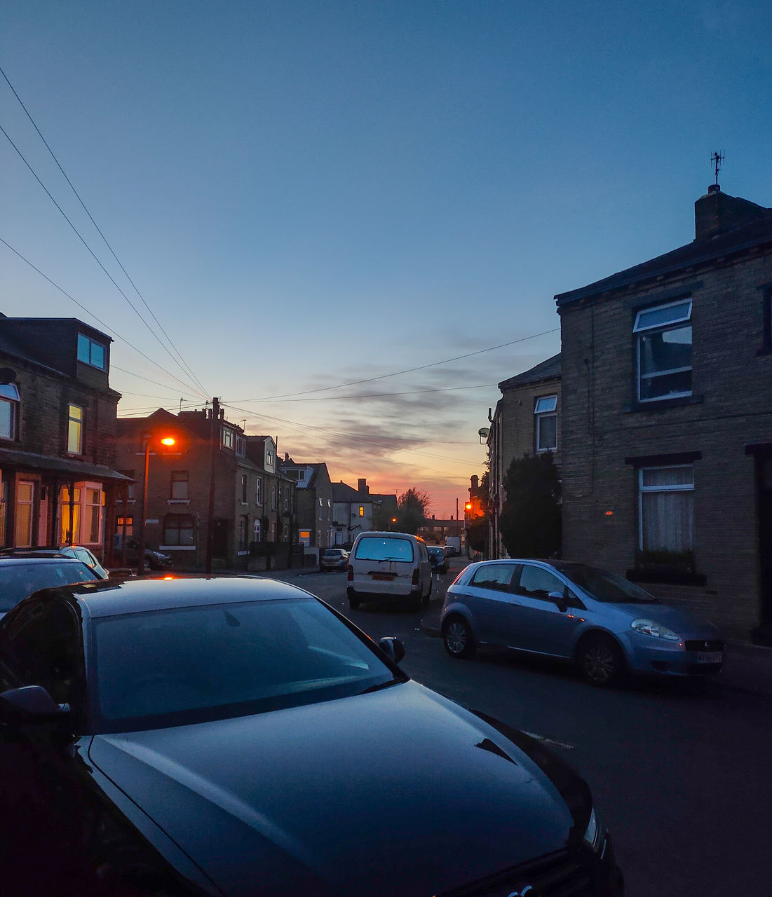 CARS ON ROAD BY BUILDINGS AGAINST SKY AT DUSK