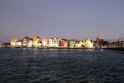 Sea by buildings against sky at dusk