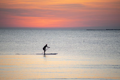 Silhouette person on sea against sky during sunset