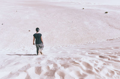 Rear view of woman walking at sandy beach on sunny day