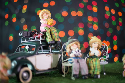 Close-up of figurines with toy car against illuminated lights