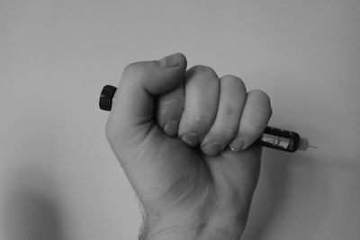 Cropped hand holding syringe against wall