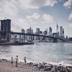 View of city at waterfront against cloudy sky