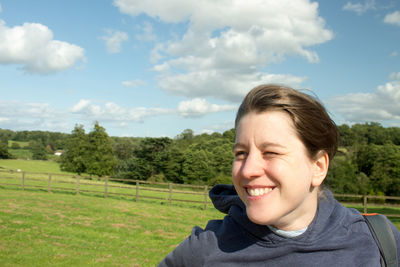Close-up of smiling woman on field against sky during sunny day