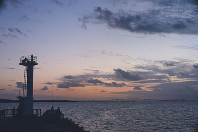 Lighthouse by sea against sky during sunset