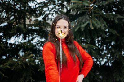 Outdoor portrait of happy cute latina girl in winter hat and red sweater posing with sparkler