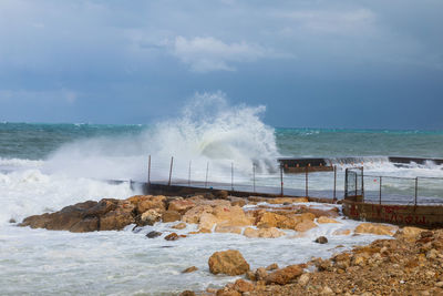 Waves splashing on rocks at shore against sky