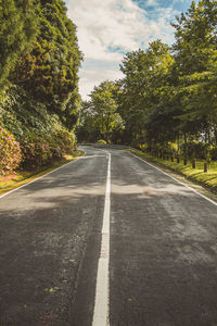 Empty road amidst trees against sky