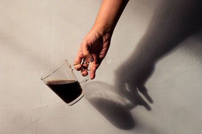 Midsection of person holding drink on table against wall