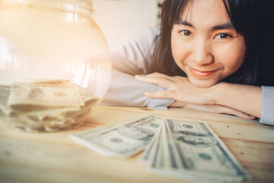 Close-up portrait of smiling young woman with paper currency on table