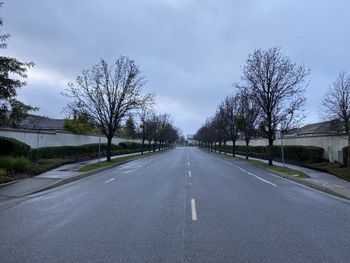 Empty road along bare trees against sky