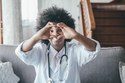 Portrait of doctor making heart shape sitting at home