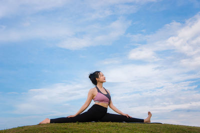 Side view of woman doing yoga on grassy field against cloudy sky