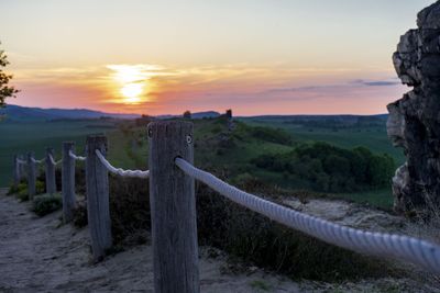 Wooden posts on landscape against sky during sunset