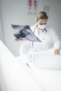 Female doctor holding medical x-ray using laptop on desk in hospital