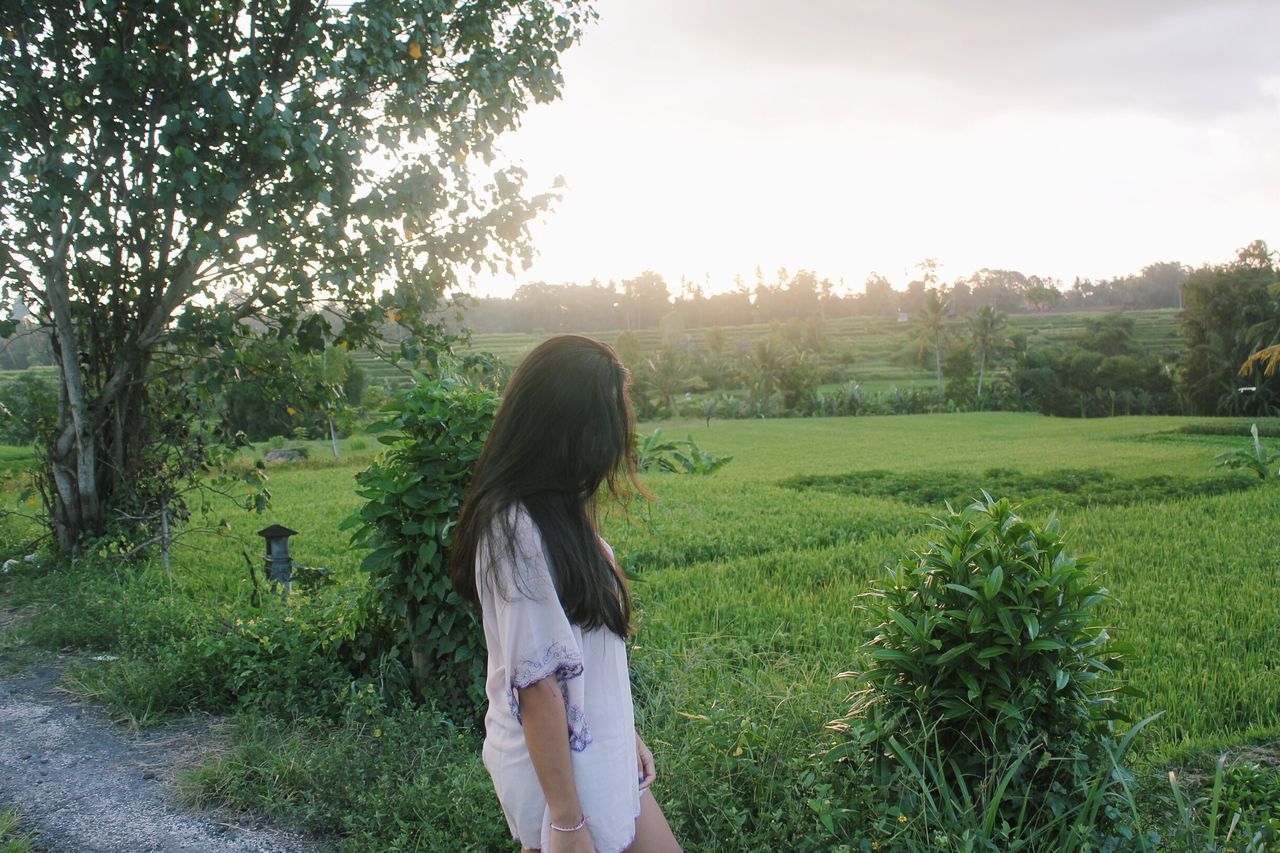 grass, tree, lifestyles, leisure activity, field, grassy, long hair, sky, nature, casual clothing, tranquility, growth, green color, outdoors, day, landscape, tranquil scene, plant, beauty in nature, scenics, park