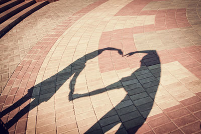 Shadow of couple making heart shape on footpath