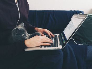 Midsection of woman with cat working on laptop at home