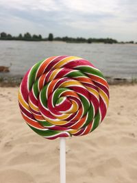 Close-up of colorful lollypop on beach against sky.