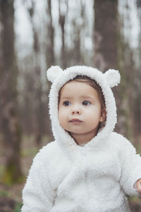 Adorable baby in a bear costume in the forest by a fallen tree