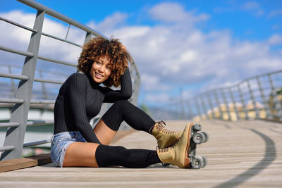 Full length of young woman with roller skates standing in circle structure against sky