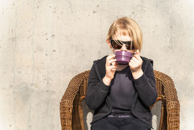 Portrait of young woman wearing sunglasses against wall