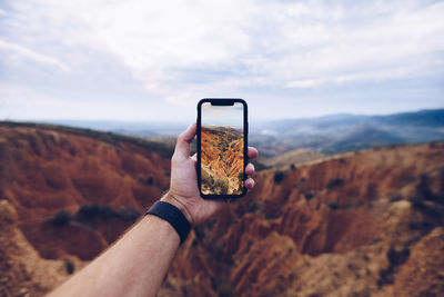 Midsection of person photographing with mobile phone against sky