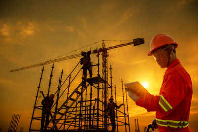 People working on construction site against sky during sunset