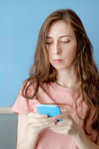 Caucasian girl with long hair in a pink t-shirt, looks at the phone. work on the phone