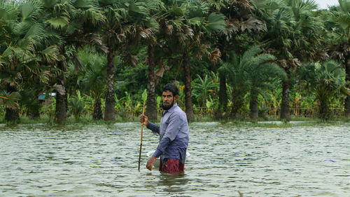 Full length of man standing on palm tree in lake