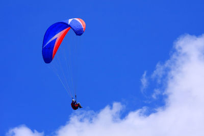 Low angle view of person paragliding against blue sky 