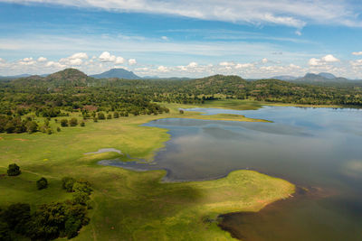 Valley with a lake and tropical vegetation against a blue sky and clouds. sorabora lake, sri lanka.