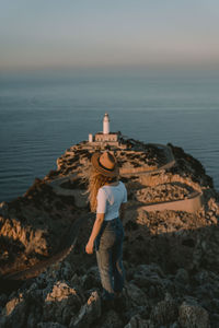 Man standing on rock by sea against sky