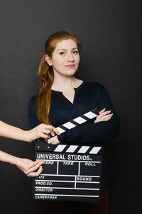 Portrait of smiling woman by cropped hands holding film slate by against black background