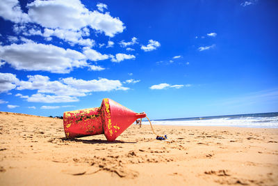 Buoy on sand at beach against sky during sunny day