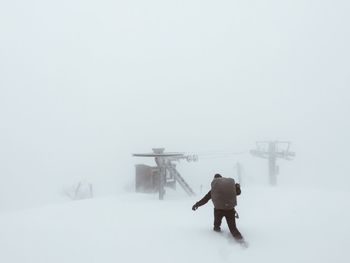 Rear view of man walking on snow covered landscape during foggy weather