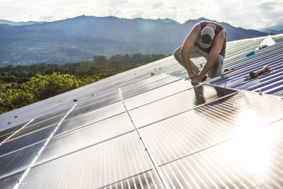 Worker uses hand tool to secure solar panels on roof of building.