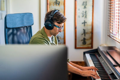 Side view of male musician in casual clothes playing melody on piano while sitting in modern apartment near window