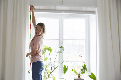 Smiling designer measuring window with tape measure at home